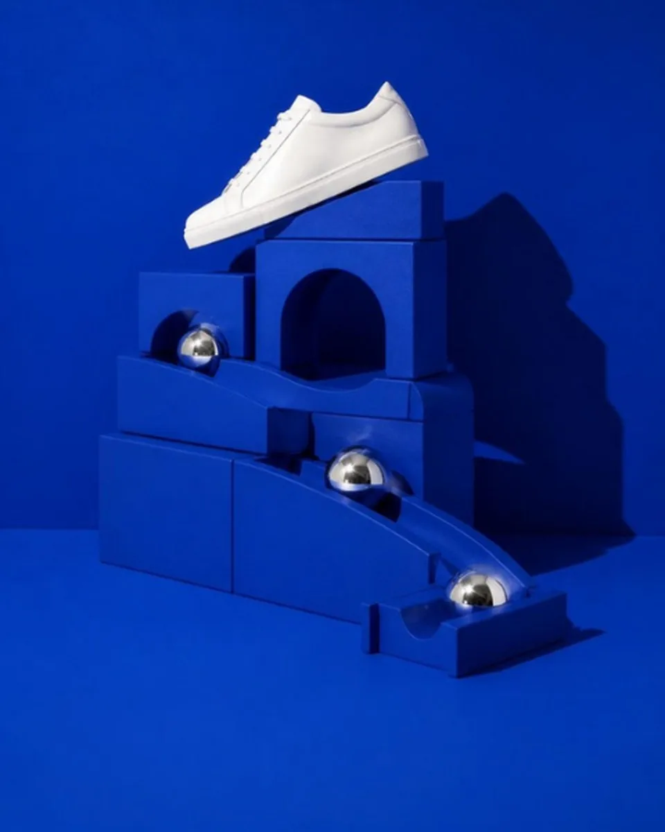 A white sneaker on top of a cobalt blue marble run, with chrome spheres rolling down the connected ramps